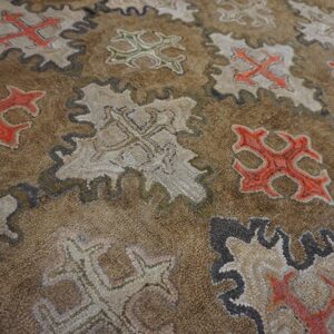 Close-up of a brown rug featuring repeating stylized cross motifs in red, white, and green within scalloped frames, by Rugs On Net