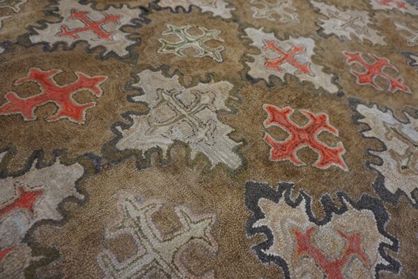 Close-up of a brown rug featuring repeating stylized cross motifs in red, white, and green within scalloped frames, by rugs on net