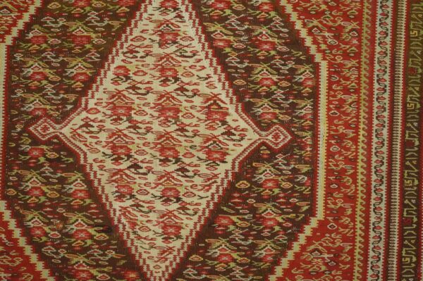 Close-up of a richly colored kilim rug featuring a central cream medallion with red floral motifs against a dark brown field, by rugs on net