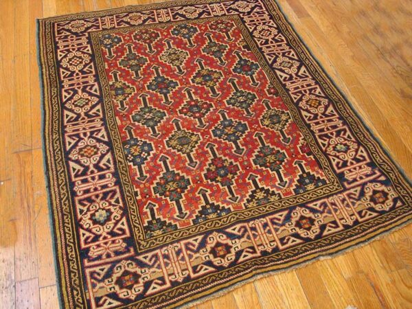 Close-up of a red field rug with geometric motifs and a dark border on a wooden floor by rugs on net
