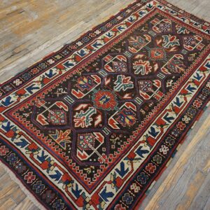 A dark, geometric Caucasian rug featuring red, blue, and cream accents on a distressed wooden floor by Rugs On Net. by Rugs On Net