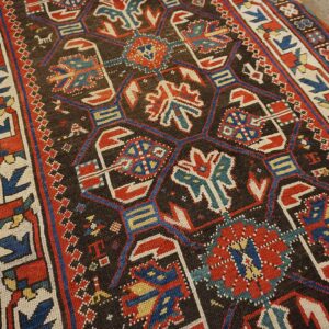 Close-up of a dark ground Caucasian rug with geometric motifs in red, blue, and cream by Rugs On Net