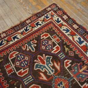 Close-up of a richly patterned antique rug with geometric motifs in red, blue, and cream on a dark brown field, resting on worn wooden floors, by Rugs On Net