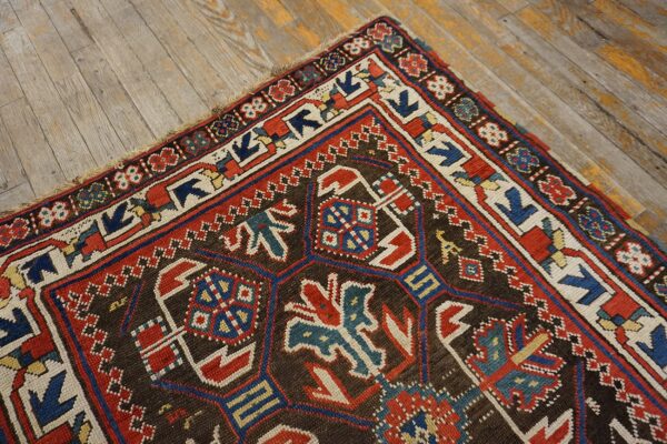 Close-up of a richly patterned antique rug with geometric motifs in red, blue, and cream on a dark brown field, resting on worn wooden floors, by rugs on net