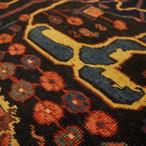 Close-up of a dark rug with geometric patterns in red, gold, and blue, showing knot detail by Rugs On Net. by Rugs On Net
