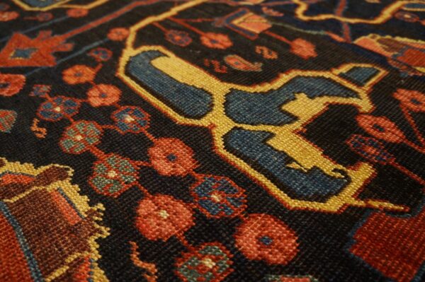 Close-up of a dark rug with geometric patterns in red, gold, and blue, showing knot detail by rugs on net. By rugs on net
