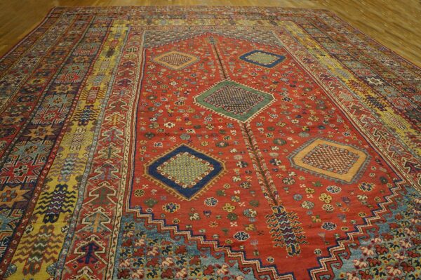 A vibrant, antique rug with a dominant red field and geometric medallions, featuring multi-colored striped borders, by rugs on net