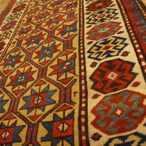 Close-up of a geometric runner rug with red, blue, and gold patterns on a wooden floor by Rugs On Net. by Rugs On Net