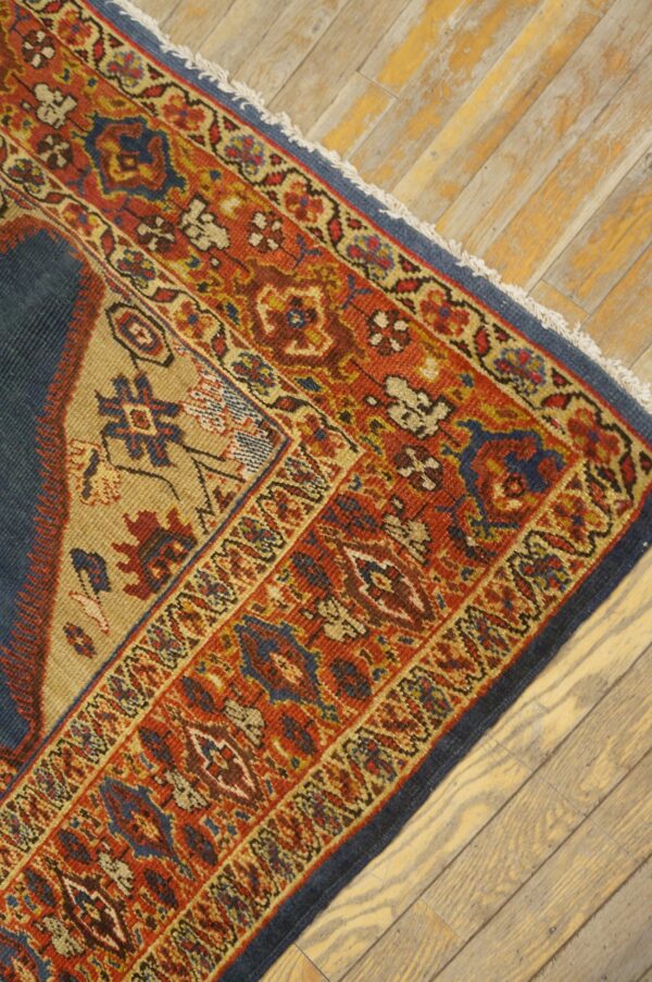 Close-up corner detail of an antique rug with rich red, blue, and tan geometric patterns resting on distressed wooden floors by rugs on net. By rugs on net