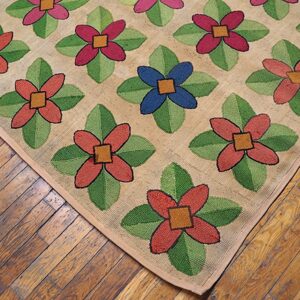 Close-up of a hooked rug with colorful floral patterns on a tan background, resting on wooden floors, by Rugs On Net