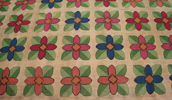 Close-up of a hooked rug featuring a repeating floral pattern with alternating red and blue flowers on a beige ground, by rugs on net. By rugs on net