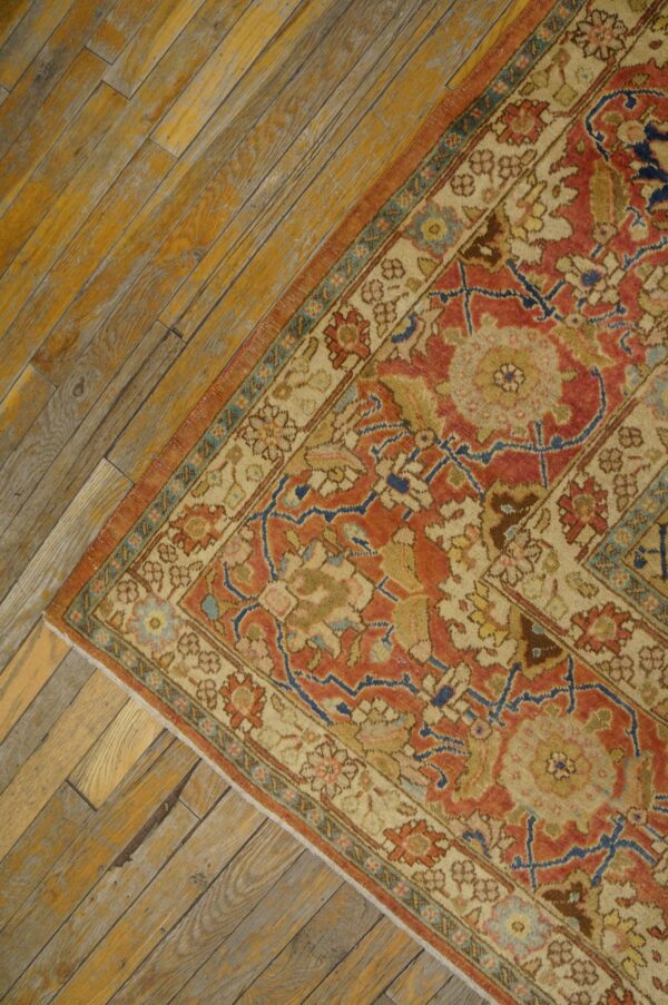 Close-up corner of an antique rug with red and beige patterns on distressed wood flooring by rugs on net