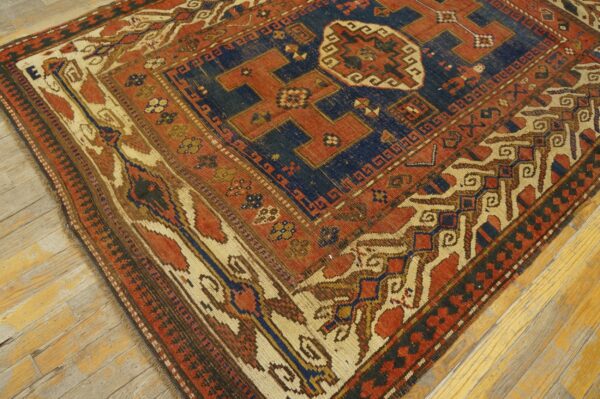 Close-up of a richly colored antique rug with geometric patterns in red, blue, and cream on a wooden floor, by rugs on net