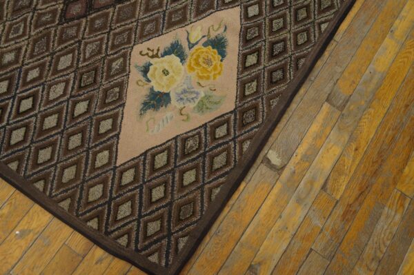 Close-up of a hooked rug with brown diamond patterns and a central floral medallion on wood flooring by rugs on net