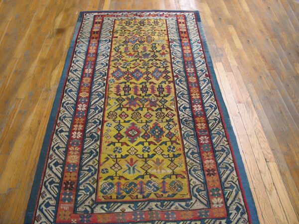 A long runner rug with a vibrant yellow field and geometric patterns in red and blue on a light wood floor by rugs on net. By rugs on net
