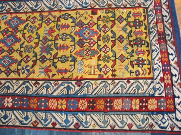 Close-up of a vibrant yellow field rug with geometric and floral motifs, bordered by intricate blue and white patterns by rugs on net. By rugs on net