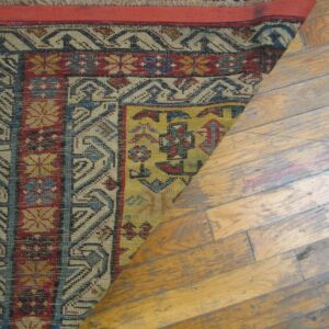 Close-up of a colorful geometric rug partially rolled back on a wooden floor, by Rugs On Net