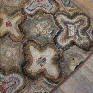 Close-up of a textured, multi-toned hooked rug featuring abstract star or cross patterns in blues, browns, and creams, resting on rustic wooden floorboards by Rugs On Net. by Rugs On Net