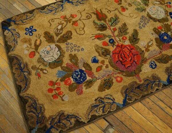 Close-up view of the textured, tan background of the antique arts and crafts floral rug, showing detailed red, blue, and white flowers and foliage on a wooden floor by rugs on net. By rugs on net