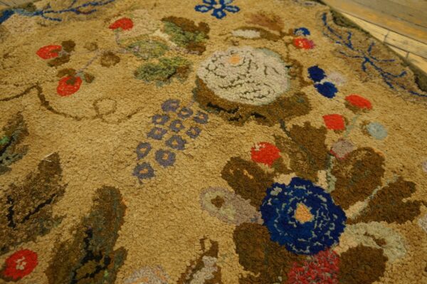 Close-up of a hooked rug with floral motifs in brown, blue, and red on a tan ground by rugs on net. By rugs on net