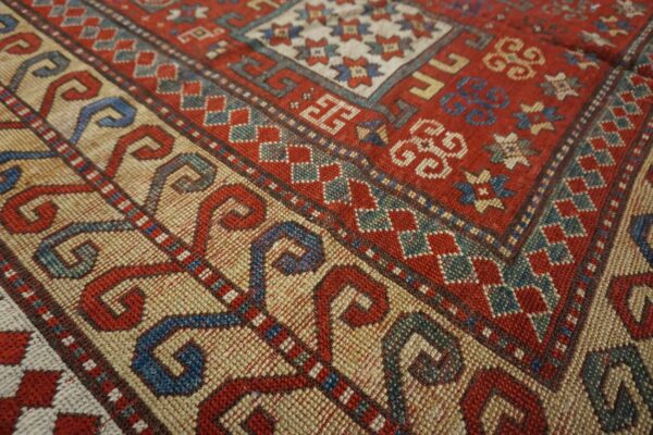 Close-up detail of the vibrant red and cream field with geometric borders of the caucasian rug by rugs on net. By rugs on net