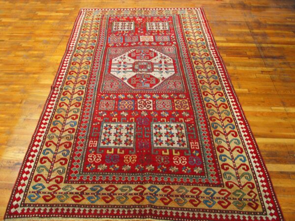 A vibrant red caucasian rug with geometric patterns on a wooden floor by rugs on net. By rugs on net