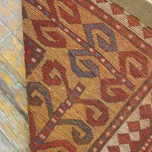 Close-up of a richly patterned rug with red and gold tones, partially rolled up, by Rugs On Net. by Rugs On Net