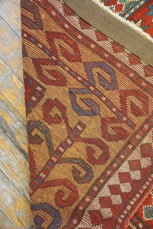 Close-up of a richly patterned rug with red and gold tones, partially rolled up, by rugs on net. By rugs on net