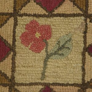 Close-up of a hooked rug featuring a central red flower motif on a tan field, framed by geometric brown and maroon shapes, by Rugs On Net