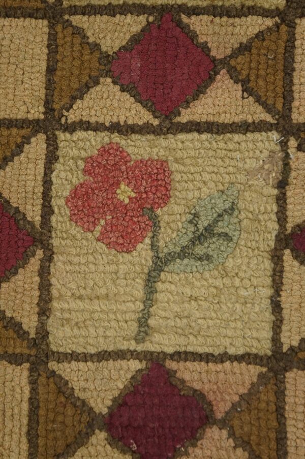 Close-up of a hooked rug featuring a central red flower motif on a tan field, framed by geometric brown and maroon shapes, by rugs on net