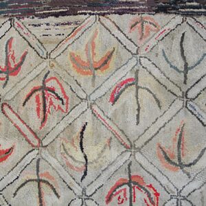 Close-up of a geometric hooked rug with abstract leaf-like motifs in red, black, and orange within diamond compartments, by Rugs On Net. by Rugs On Net
