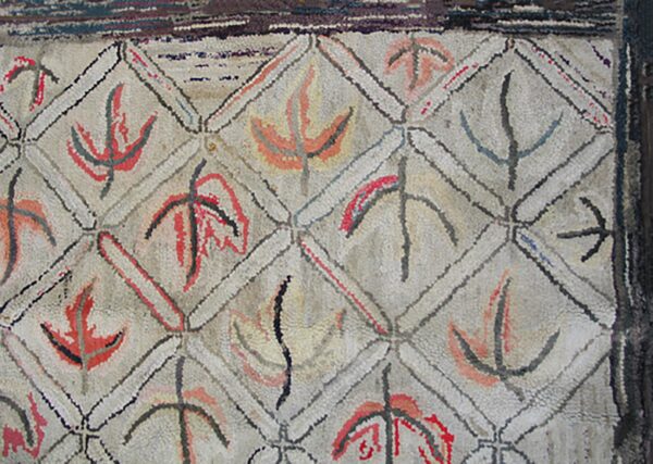 Close-up of a geometric hooked rug with abstract leaf-like motifs in red, black, and orange within diamond compartments, by rugs on net. By rugs on net