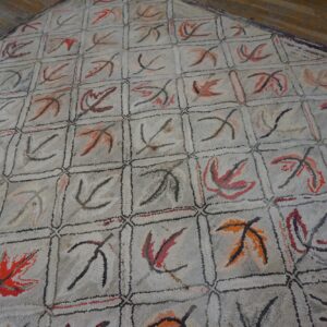 Close-up of a light-colored rug with a grid pattern featuring abstract leaf motifs in red, orange, and black, by Rugs On Net
