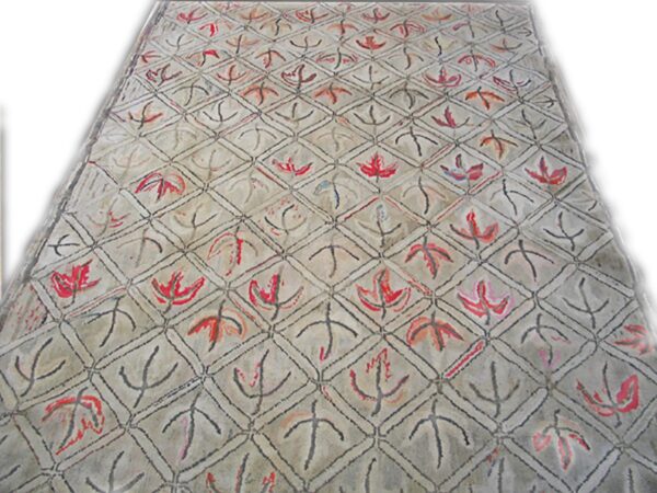 A close-up view of a light-colored rug featuring a repeating diamond lattice pattern with stylized red and black leaf motifs, by rugs on net. By rugs on net