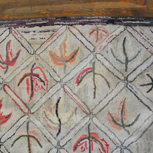 Close-up of a beige hooked rug with a repeating diamond lattice pattern filled with abstract, stylized leaf shapes in red, orange, and gray, by Rugs On Net. by Rugs On Net