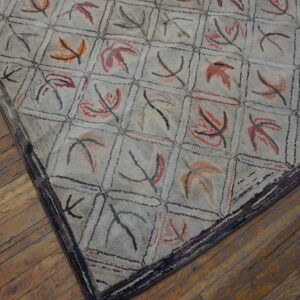Close-up view of a hooked rug with a pale background and a grid pattern containing abstract leaf shapes in muted reds and oranges, by Rugs On Net. by Rugs On Net