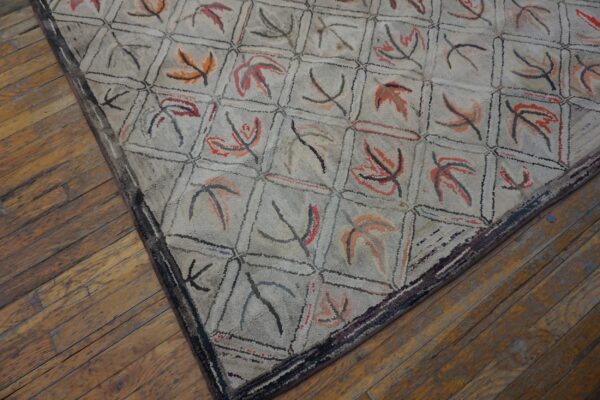 Close-up view of a hooked rug with a pale background and a grid pattern containing abstract leaf shapes in muted reds and oranges, by rugs on net. By rugs on net