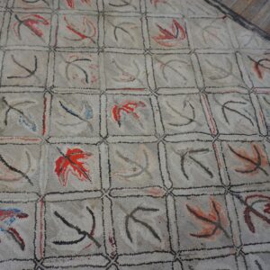 Close-up of a light gray hooked rug featuring a grid pattern with abstract leaf motifs in red and black, by Rugs On Net