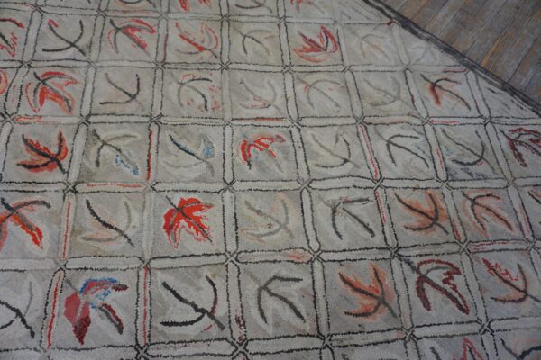 Close-up of a light gray hooked rug featuring a grid pattern with abstract leaf motifs in red and black, by rugs on net