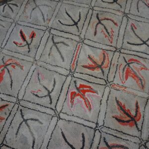 Close-up of a vintage hooked rug featuring a repeating geometric pattern with stylized red and black leaves on a light gray background, by Rugs On Net