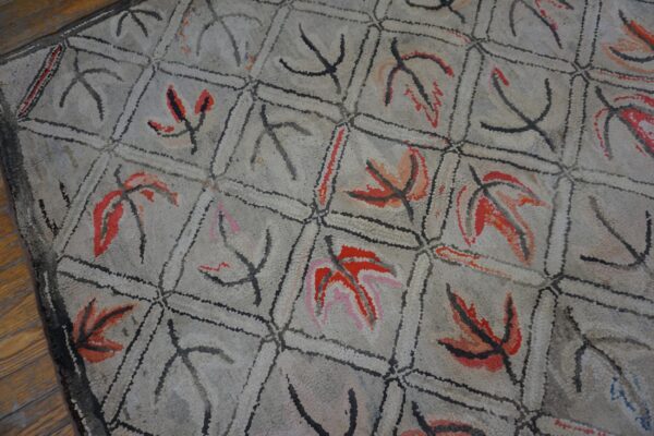 Close-up of a vintage hooked rug featuring a repeating geometric pattern with stylized red and black leaves on a light gray background, by rugs on net