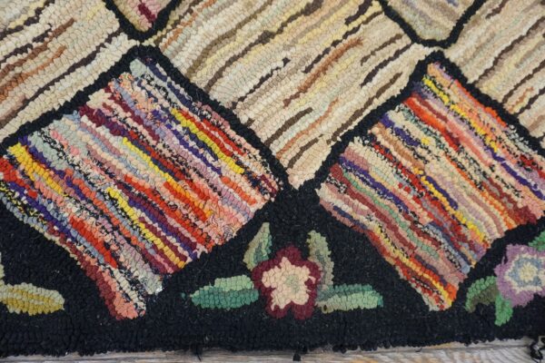 Close-up of a colorful hooked rug pattern with geometric shapes and floral accents on a black background, by rugs on net