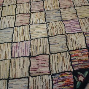 Close-up of a hooked rug featuring a patchwork of light-colored, textured squares outlined in black, with some colorful accent squares and floral border details on a dark background, by Rugs On Net