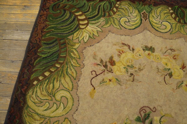 Close-up of a hooked rug featuring green foliage border and yellow floral center on a tan field, by rugs on net. By rugs on net