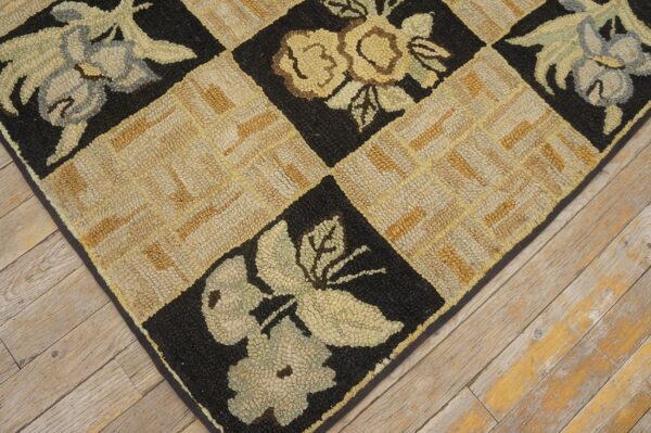 Close-up of a hooked rug with a checkerboard pattern featuring floral motifs in black squares and a tan geometric weave in between, by rugs on net. By rugs on net