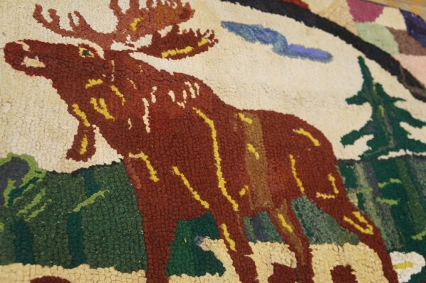 Close-up of a hooked rug featuring a large brown moose against a light background with green foliage, by rugs on net. By rugs on net