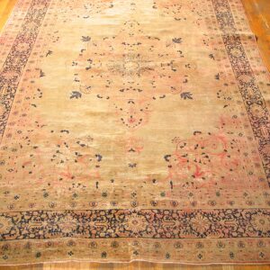 A wide shot of an antique Persian rug with faded gold and pink tones and dark blue accents, by Rugs On Net. by Rugs On Net