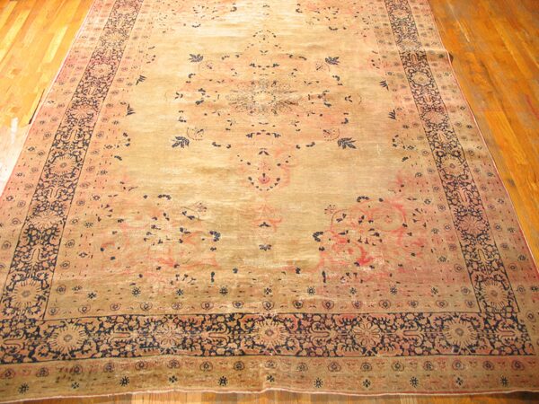 A wide shot of an antique persian rug with faded gold and pink tones and dark blue accents, by rugs on net. By rugs on net