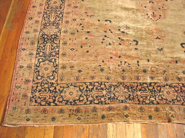 Close-up of a worn, antique rug border with navy blue floral details on a faded gold and tan field, by rugs on net