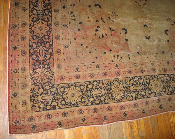 Close-up corner detail of an antique rug with faded earth tones and dark blue floral borders by rugs on net. By rugs on net